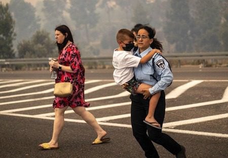 An Israeli police officer evacuates a child from the wildfires. (Israel Police/X)