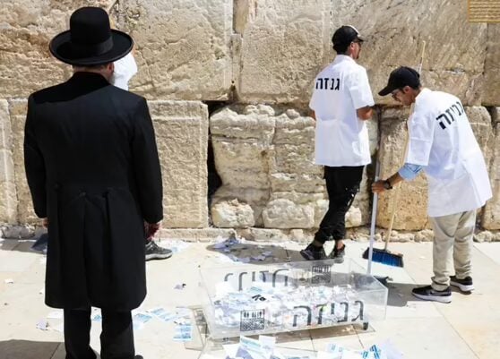Western_Wall_Cleanup Rabbi Shmuel Rabinowitz looks on as the Western Wall is cleaned ahead of Rosh Hashanah. The words on the cleaners’ jackets and on the recep- tacle is ‘Genizah,’ a term for the burial of holy items. (Western Wall Heritage Foundation)