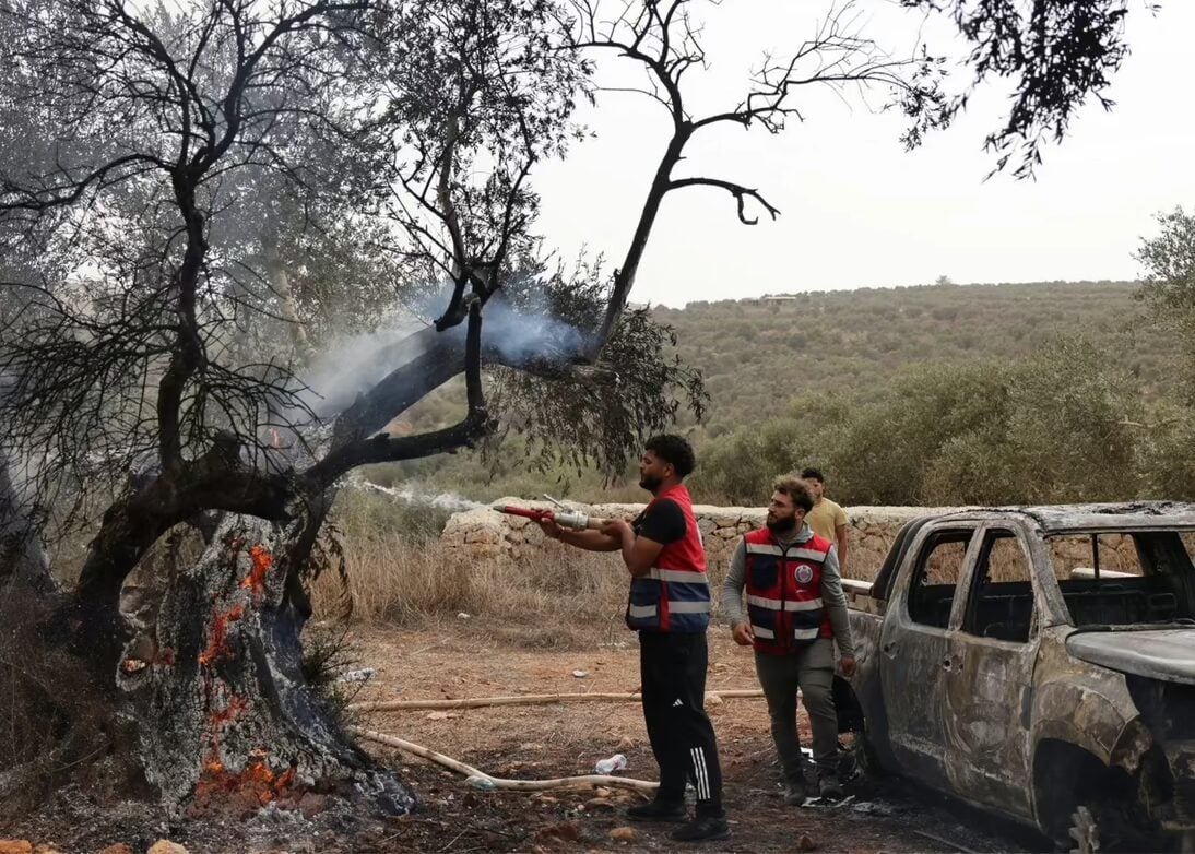 Palestinian volunteers douse an olive tree set alight along with a Palestinian-owned vehicle, reportedly by Israeli settlers, near the village of Turmus Ayya in the West Bank on Oct. 16, 2026. (Ahmad Gharabli/AFP/Getty Images)